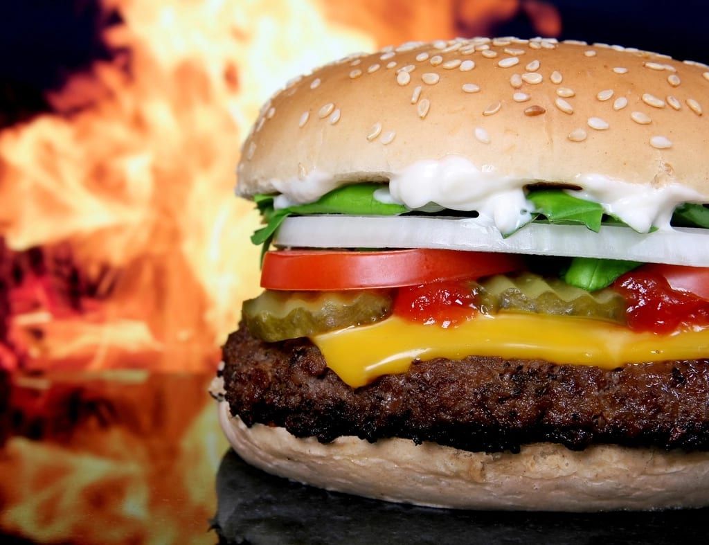 A cheeseburger in front of a wall of flame