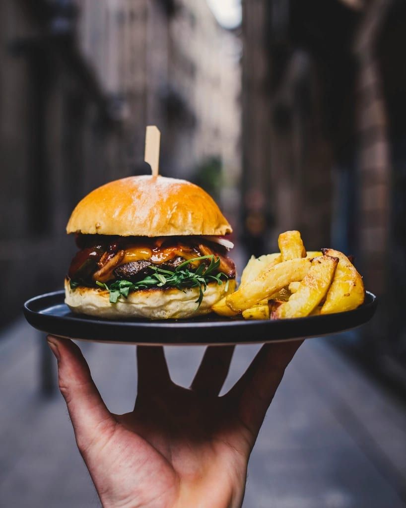 A burger and fries on a plate held out by a server
