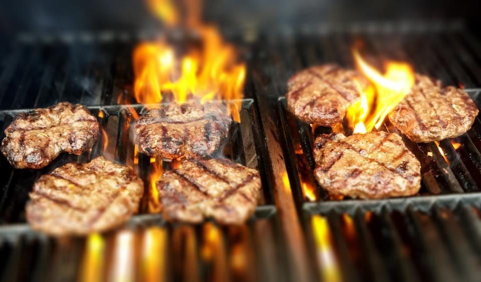 Burger patties searing over open flames on a grill